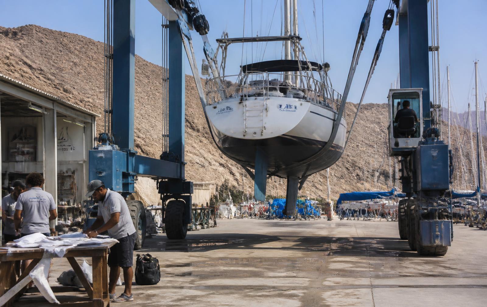 Technicians and a travel lift servicing a sailing yacht in an Omani boat yard